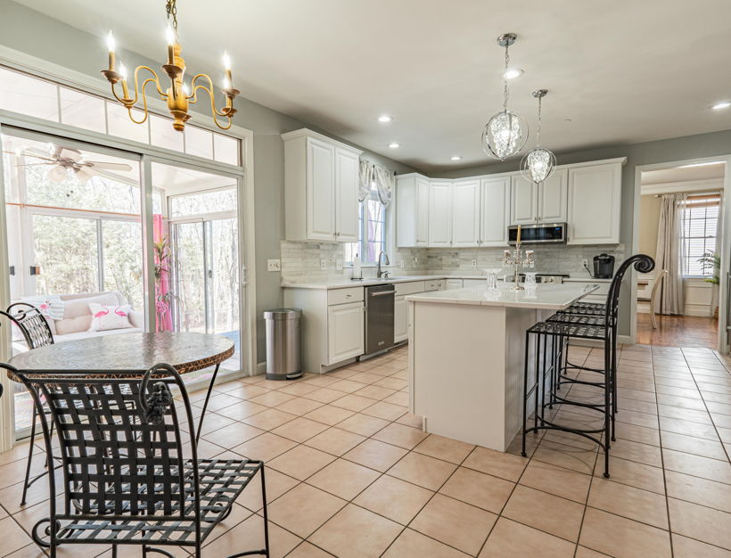 kitchen featuring natural light, a ceiling fan with notable chandelier, a breakfast bar area, a center island, refrigerator, dishwasher, microwave, light stone countertops, white cabinets, pendant lighting, and light tile flooring