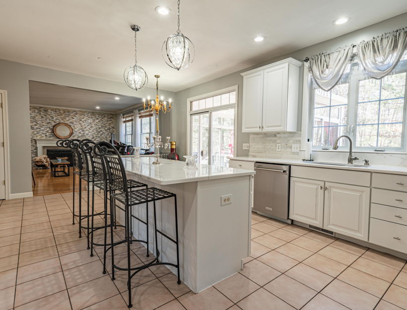 kitchen featuring natural light, a kitchen bar, a fireplace, a center island, dishwasher, light stone countertops, pendant lighting, white cabinets, and light tile floors