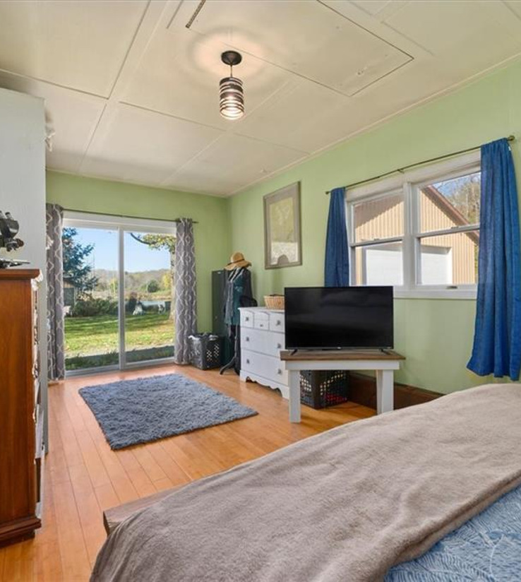 hardwood floored bedroom with multiple windows and TV