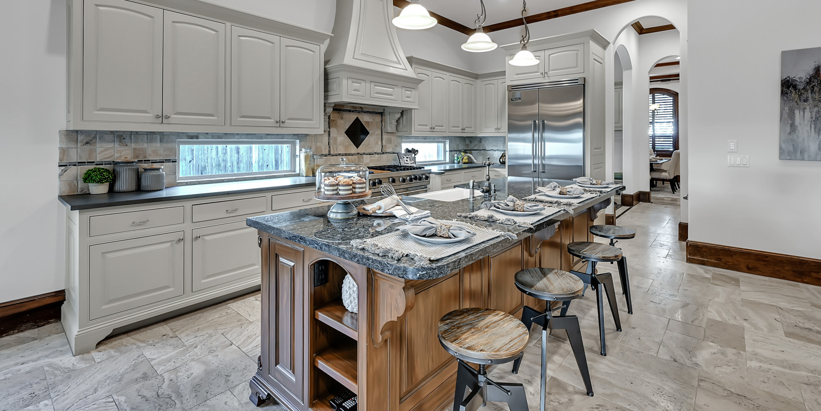 kitchen with a center island, a breakfast bar area, wood beam ceiling, natural light, stainless steel finishes, fume extractor, light floors, dark stone countertops, white cabinetry, and pendant lighting